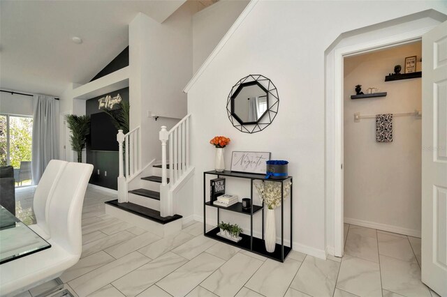 corridor with light marble finish flooring, stairway, vaulted ceiling, and baseboards