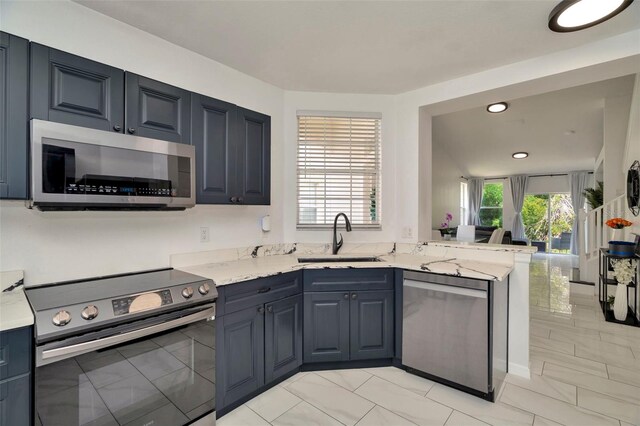 kitchen with stainless steel appliances, a sink, light marble finish floors, light stone countertops, and a peninsula