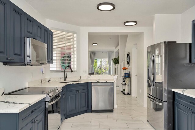 kitchen featuring stainless steel appliances, a sink, blue cabinets, and light stone counters