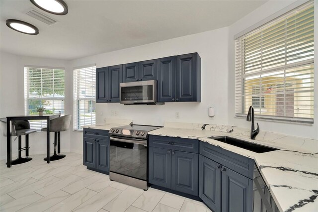 kitchen with appliances with stainless steel finishes, a sink, and light stone countertops