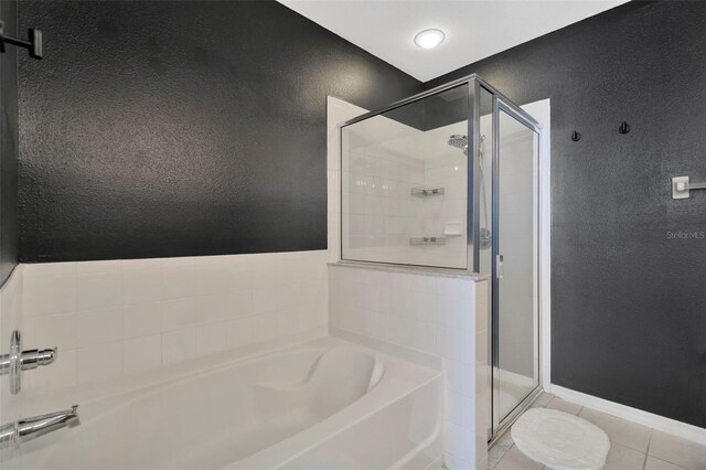 bathroom with a bath, a stall shower, tile patterned floors, a textured wall, and baseboards