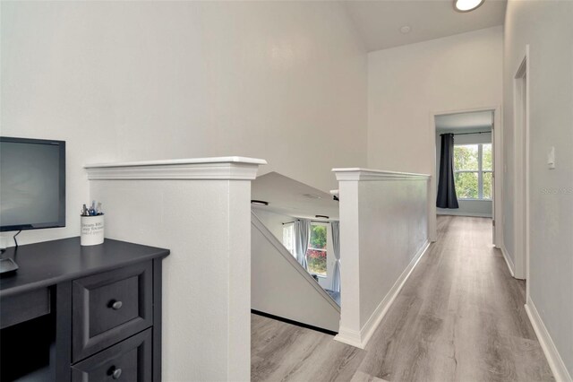 corridor featuring an upstairs landing, light wood-type flooring, and baseboards