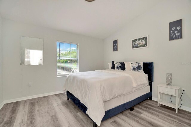 bedroom with wood finished floors, vaulted ceiling, and baseboards