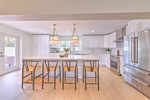 kitchen featuring light countertops, wall chimney exhaust hood, white cabinetry, light wood finished floors, and stainless steel appliances