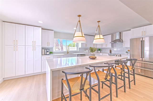 kitchen featuring appliances with stainless steel finishes, a sink, light countertops, light wood-style floors, and wall chimney exhaust hood