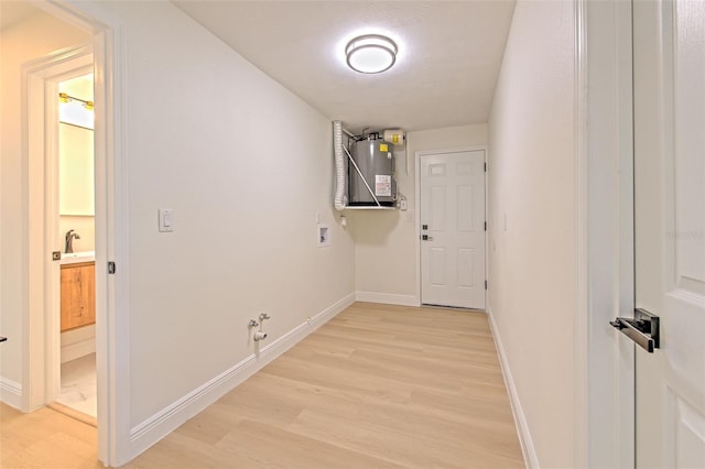 corridor with a sink, baseboards, light wood-type flooring, and electric water heater
