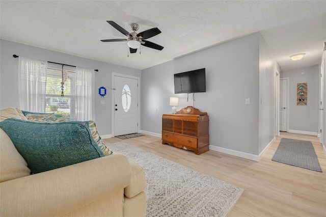 living room with ceiling fan, a textured ceiling, baseboards, and wood finished floors