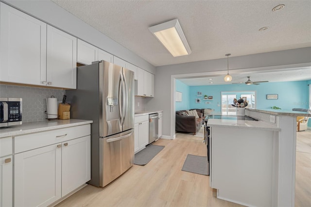 kitchen featuring stainless steel appliances, backsplash, open floor plan, and light wood-type flooring