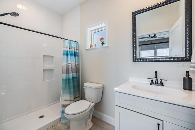 bathroom with toilet, wood finished floors, vanity, baseboards, and a tile shower