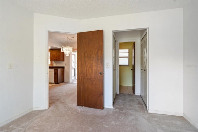 spare room featuring an inviting chandelier, light carpet, and baseboards