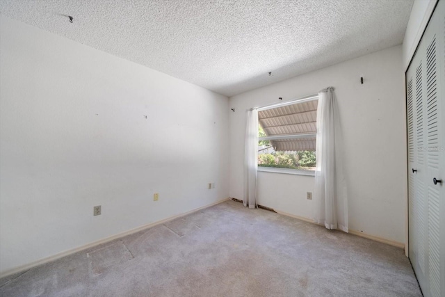 empty room featuring a textured ceiling, carpet flooring, and baseboards