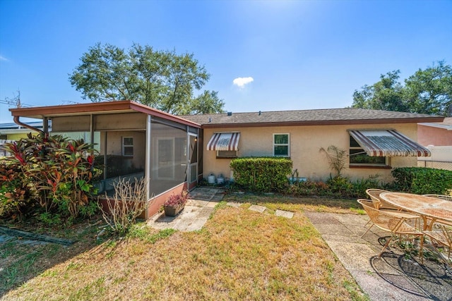 rear view of house with a sunroom, stucco siding, a lawn, and a patio area