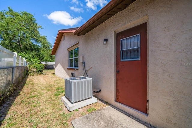 property entrance featuring a yard, fence, stucco siding, and cooling unit