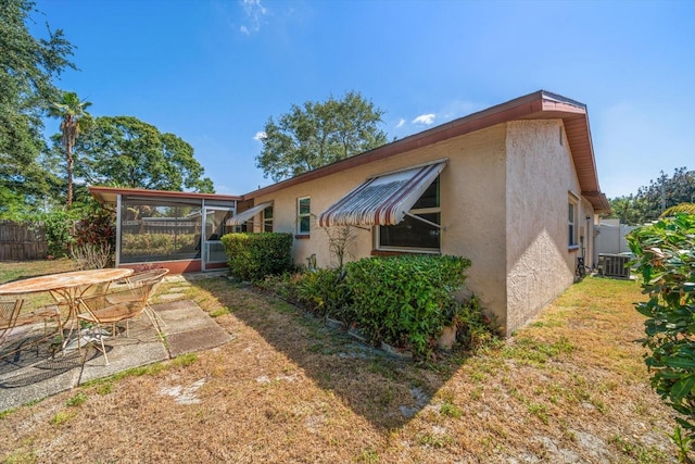 view of side of property with fence, central AC, a yard, stucco siding, and a sunroom