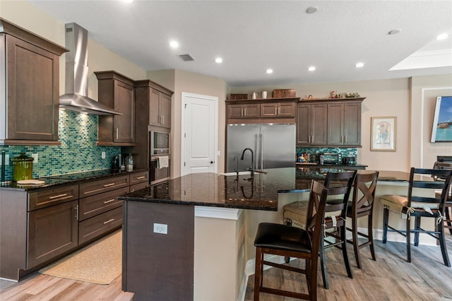 7340 W Dr, Wesley Chapel, FL 33544 - kitchen featuring built in appliances, visible vents, wall chimney exhaust hood, light wood-style flooring, and dark brown cabinets