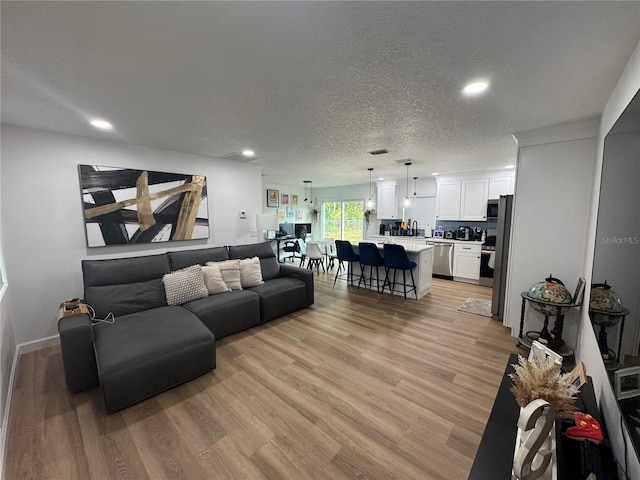 living area with light wood-style floors, baseboards, recessed lighting, and a textured ceiling