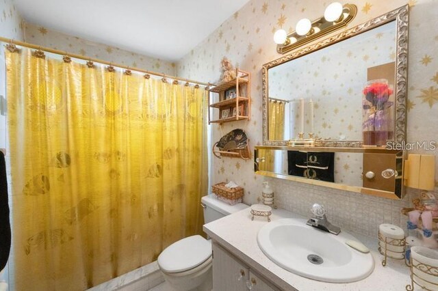 5925 Shore Blvd S Unit 602, Gulfport, FL 33707 - bathroom with toilet, wallpapered walls, a shower with shower curtain, decorative backsplash, and vanity