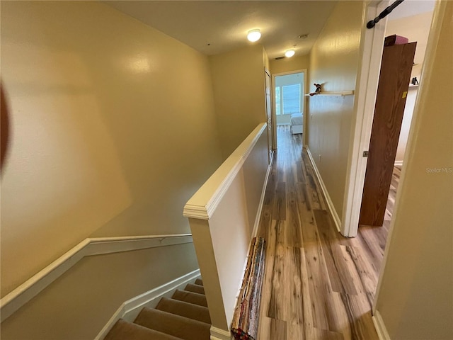 corridor with wood finished floors, baseboards, and an upstairs landing