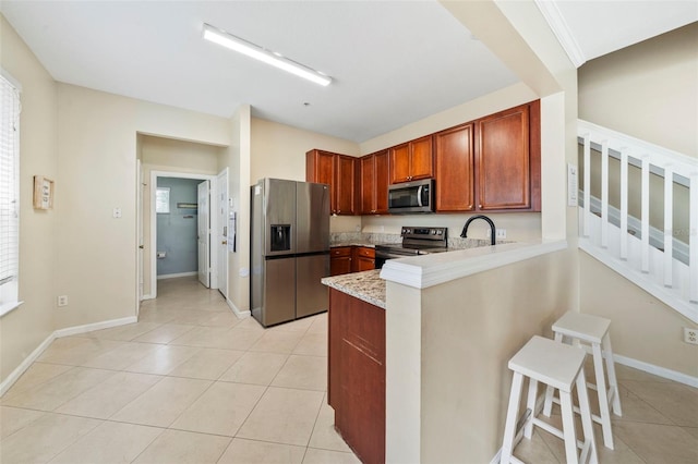 kitchen with appliances with stainless steel finishes, a peninsula, light tile patterned floors, a breakfast bar area, and baseboards
