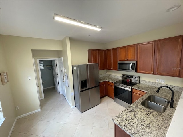 kitchen featuring stainless steel appliances, a sink, light tile patterned flooring, light stone countertops, and baseboards