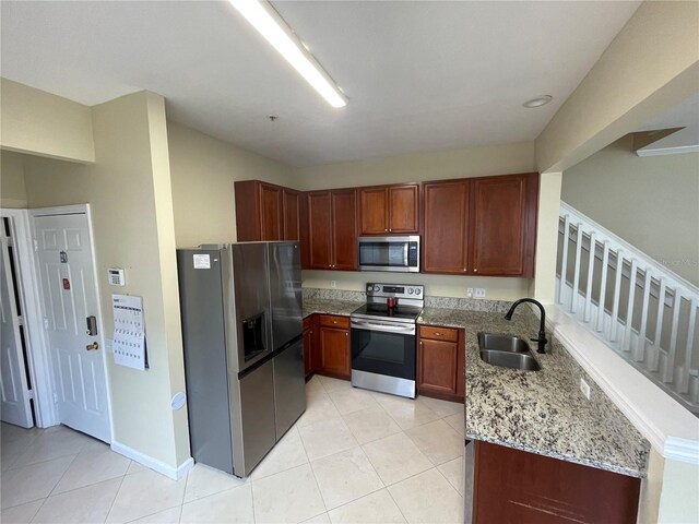 kitchen with appliances with stainless steel finishes, a sink, light tile patterned floors, and light stone counters