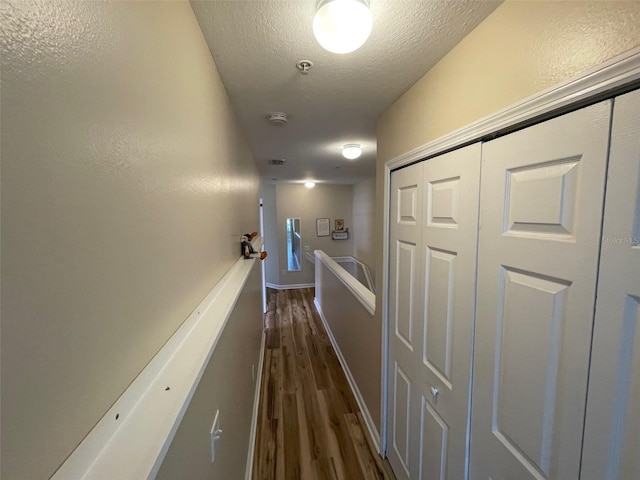 hall featuring dark wood finished floors, a textured ceiling, baseboards, and an upstairs landing