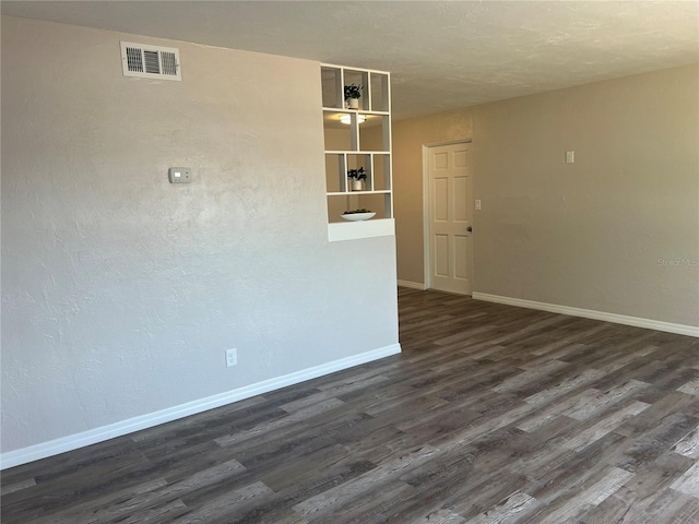 empty room featuring dark wood finished floors, visible vents, and baseboards