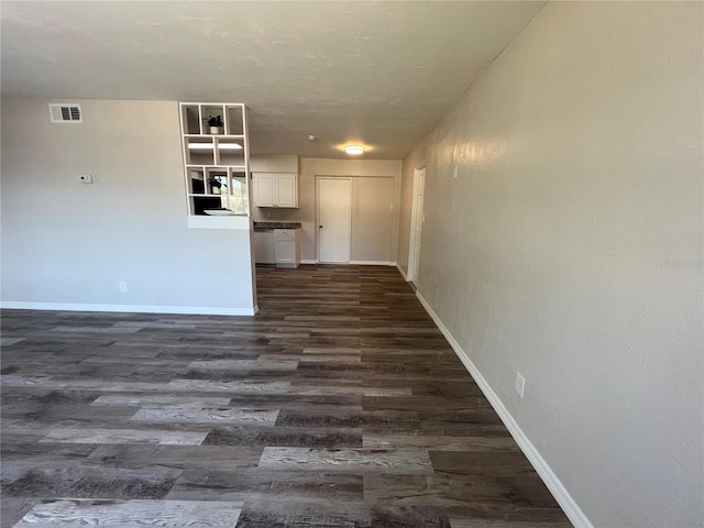 unfurnished living room featuring baseboards, dark wood-type flooring, and visible vents