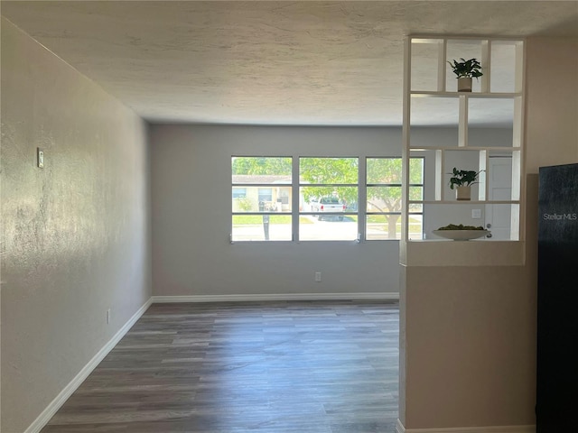 unfurnished living room featuring a textured ceiling, wood finished floors, and baseboards