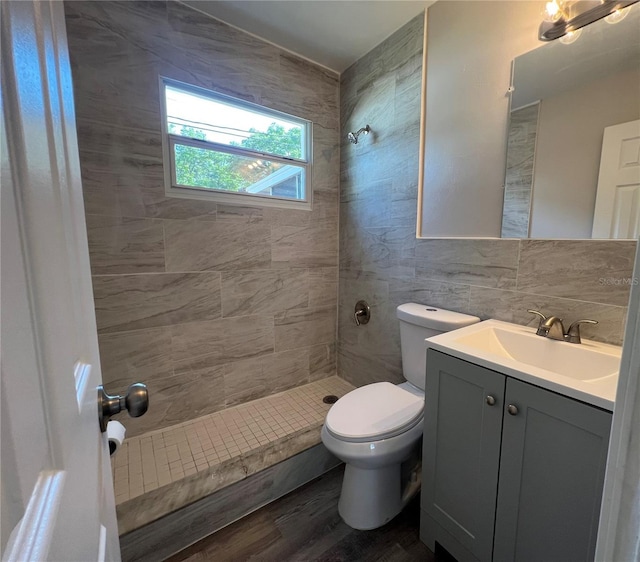 bathroom featuring toilet, tile walls, wood finished floors, vanity, and a tile shower