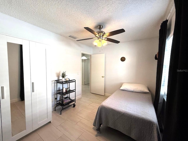 bedroom with a textured ceiling, visible vents, and ceiling fan
