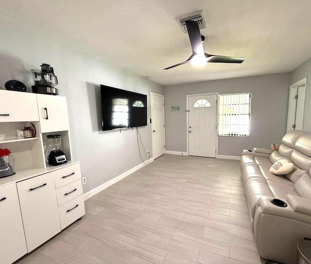 living area featuring visible vents, baseboards, ceiling fan, and light wood finished floors