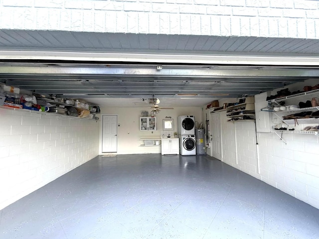 garage featuring concrete block wall, water heater, a ceiling fan, and stacked washer and dryer