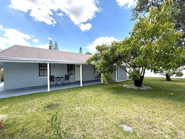 rear view of house with a lawn, concrete block siding, and roof with shingles