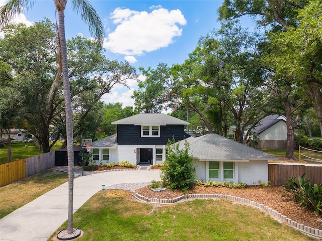 view of front of property with concrete driveway, roof with shingles, fence, and a front yard