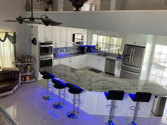 11727 Spanish Lake Dr, Tampa, FL 33635 - kitchen with light stone countertops, a sink, stainless steel appliances, white cabinetry, and a kitchen bar