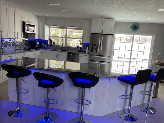 11727 Spanish Lake Dr, Tampa, FL 33635 - kitchen featuring visible vents, a sink, dark stone countertops, stainless steel appliances, and white cabinetry