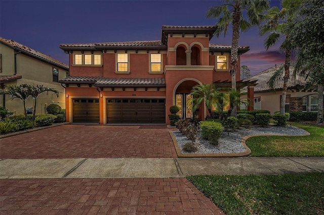 mediterranean / spanish-style house with stucco siding, a garage, a tiled roof, and decorative driveway