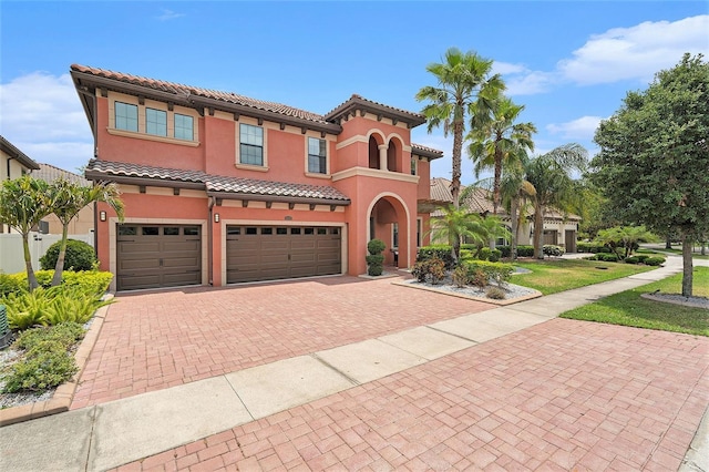 mediterranean / spanish house with stucco siding, a tiled roof, a garage, and decorative driveway
