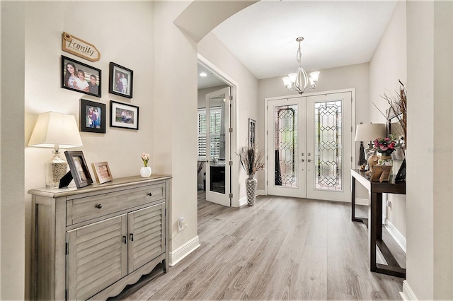foyer entrance featuring french doors, a chandelier, light wood-style flooring, arched walkways, and baseboards