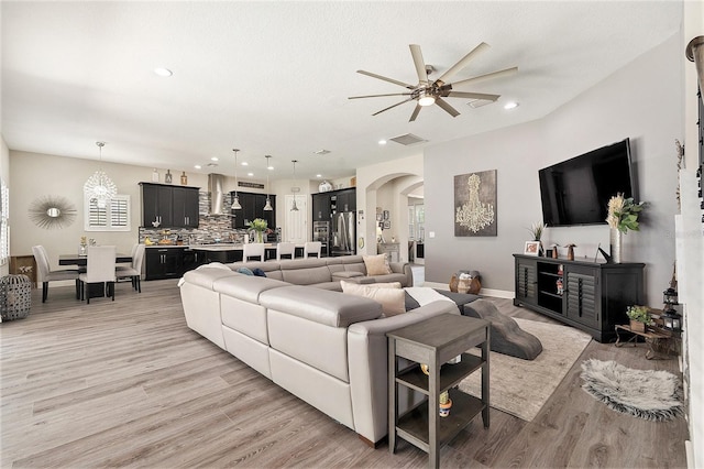living area with ceiling fan with notable chandelier, visible vents, arched walkways, light wood-style floors, and recessed lighting