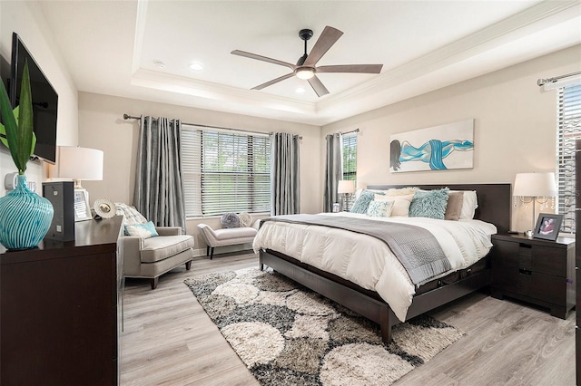 bedroom featuring a tray ceiling, light wood finished floors, ornamental molding, and multiple windows
