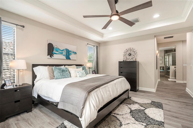 bedroom featuring light wood-style flooring, baseboards, visible vents, crown molding, and a raised ceiling