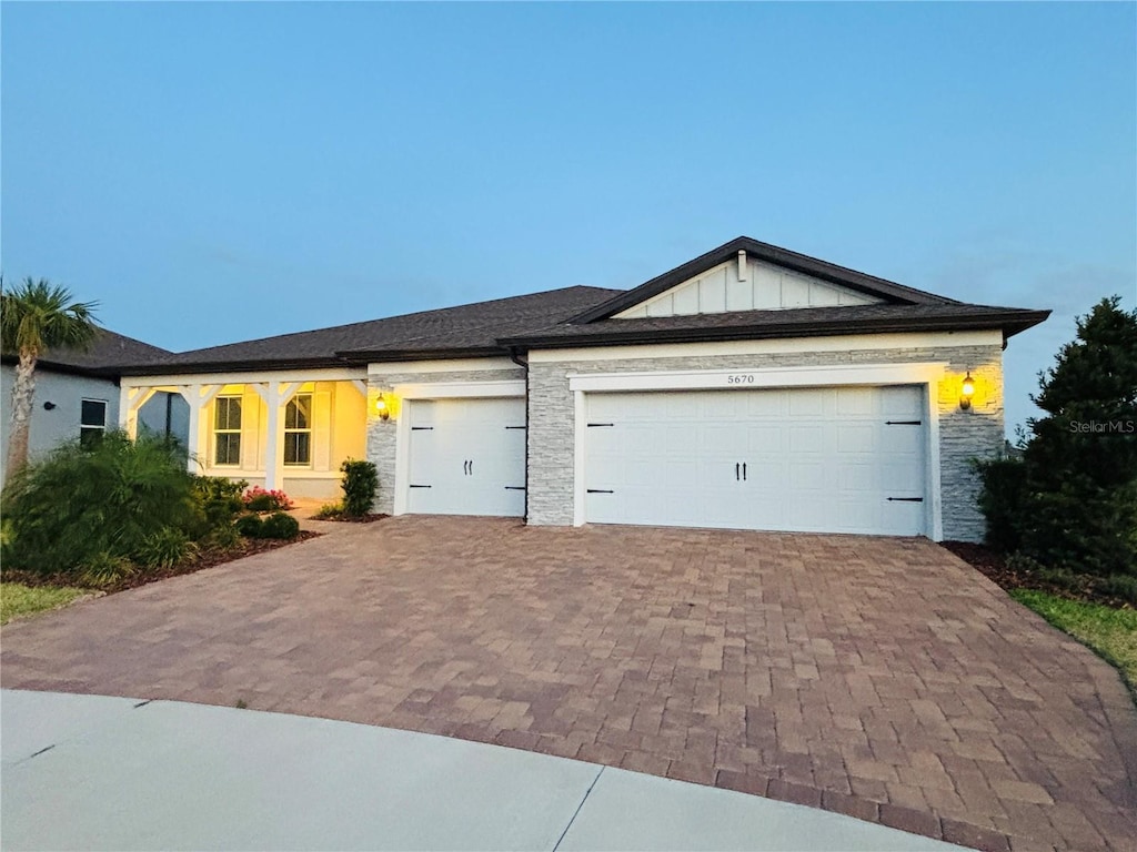 ranch-style house featuring board and batten siding, a garage, stone siding, and decorative driveway