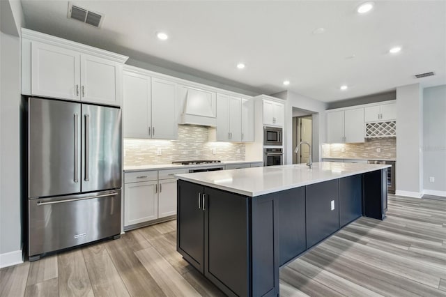 5670 Shorebird Br, Land O Lakes, FL 34638 - kitchen with stainless steel appliances, custom range hood, white cabinetry, tasteful backsplash, and light wood-type flooring