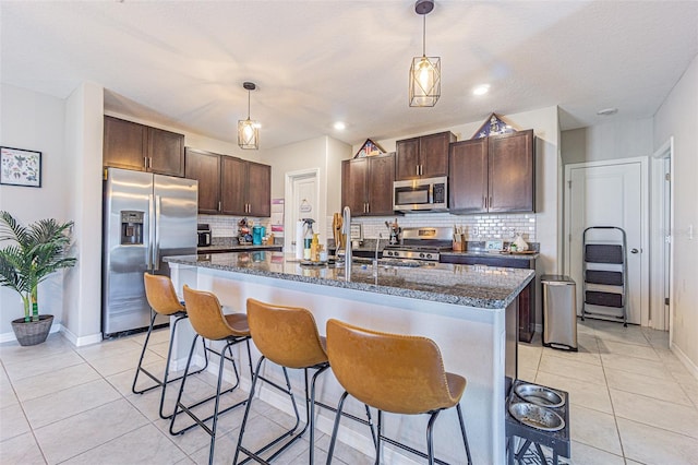 kitchen with dark brown cabinets, a breakfast bar, appliances with stainless steel finishes, decorative backsplash, and light tile patterned flooring