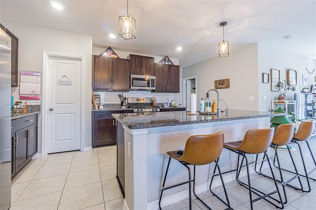 kitchen with pendant lighting, backsplash, a kitchen bar, dark brown cabinets, and appliances with stainless steel finishes