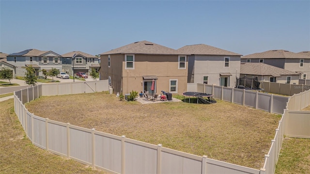 rear view of house with a trampoline, a residential view, stucco siding, a fenced backyard, and a lawn