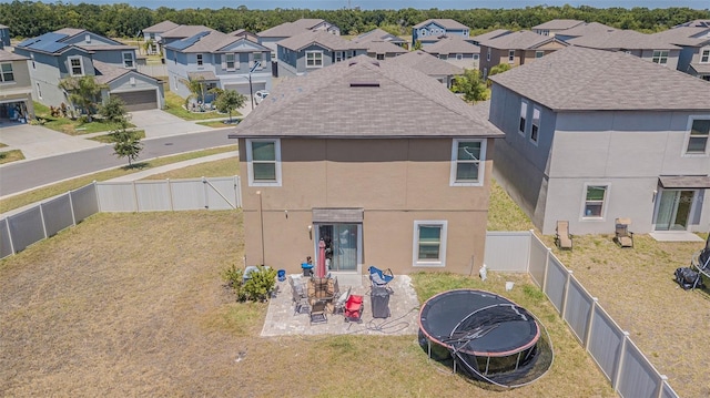 back of property featuring a residential view, a trampoline, stucco siding, a lawn, and a fenced backyard