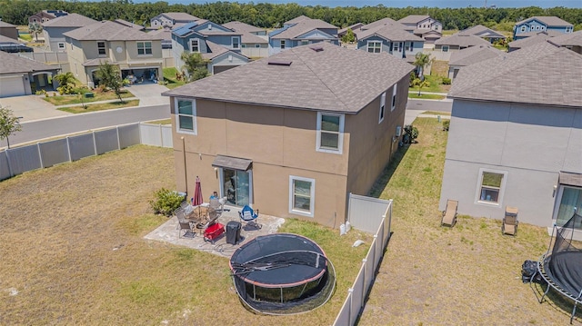 rear view of house with a trampoline, stucco siding, a residential view, and a fenced backyard